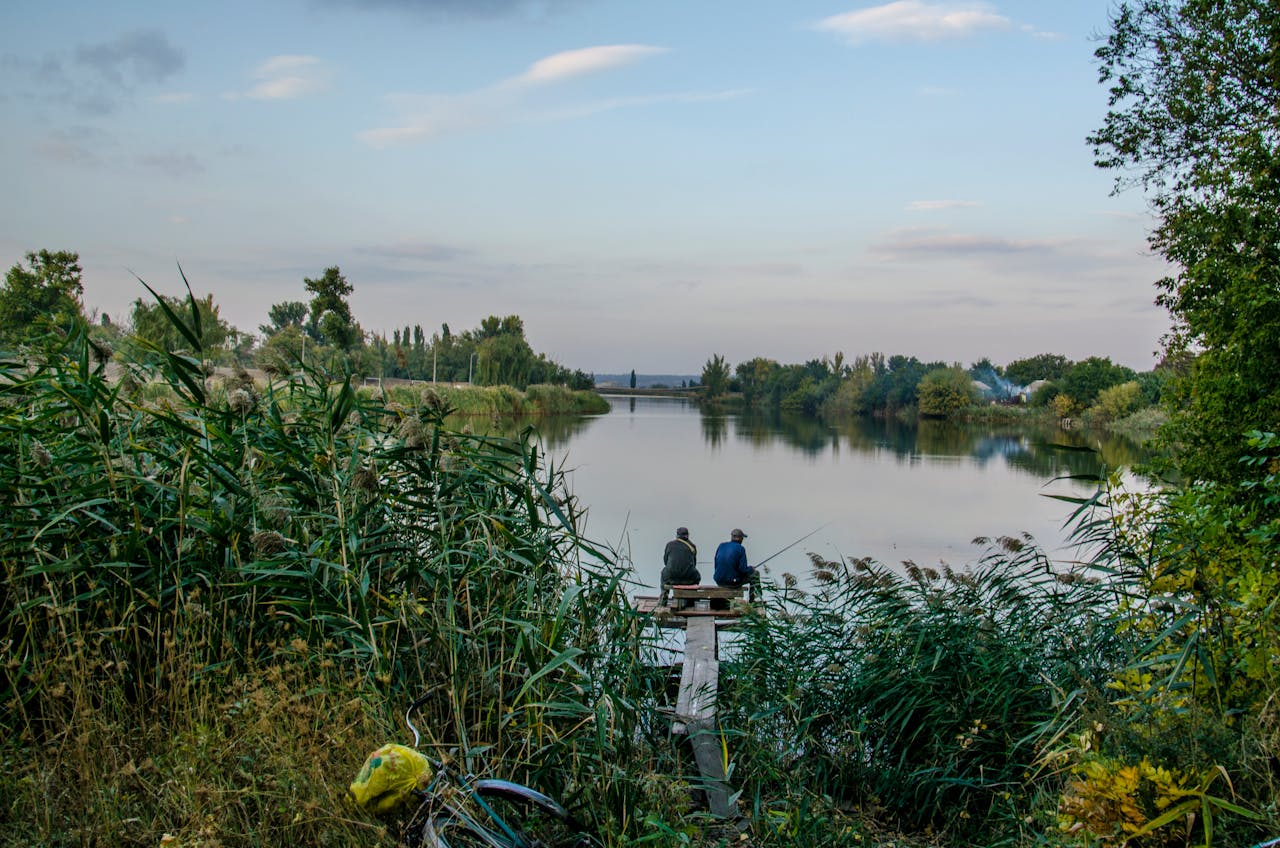 Two men fishing on a tranquil Ukrainian river, surrounded by nature's beauty at dusk.